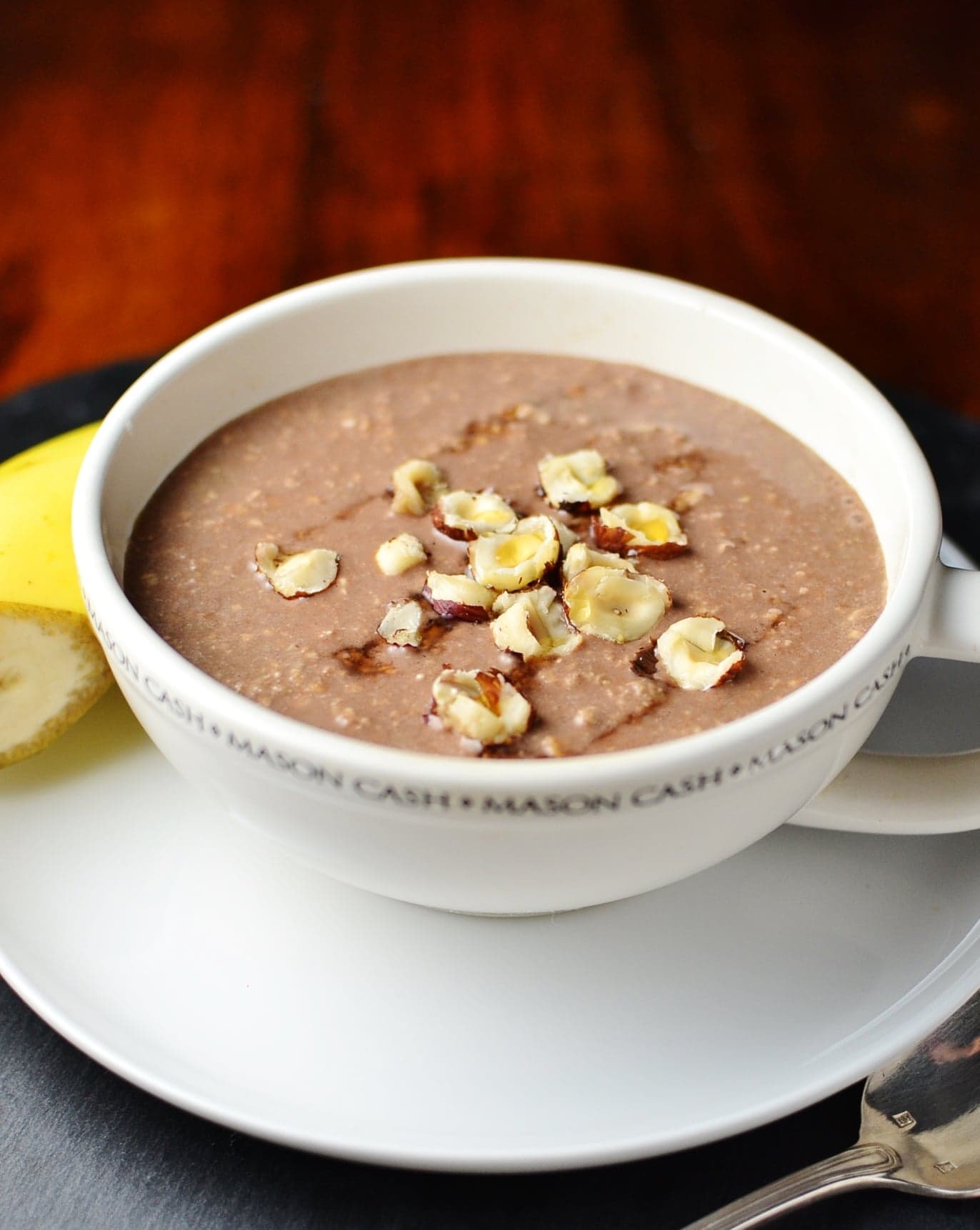 Mocha overnight oats in coffee cup on top of saucer with half banana in background.
