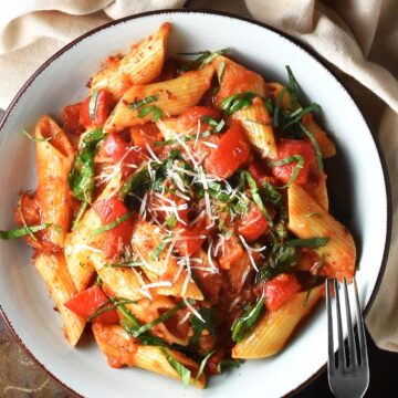 Top down view of pepper tomato pasta sauce with rigatoni pasta in blue bowl with fork.