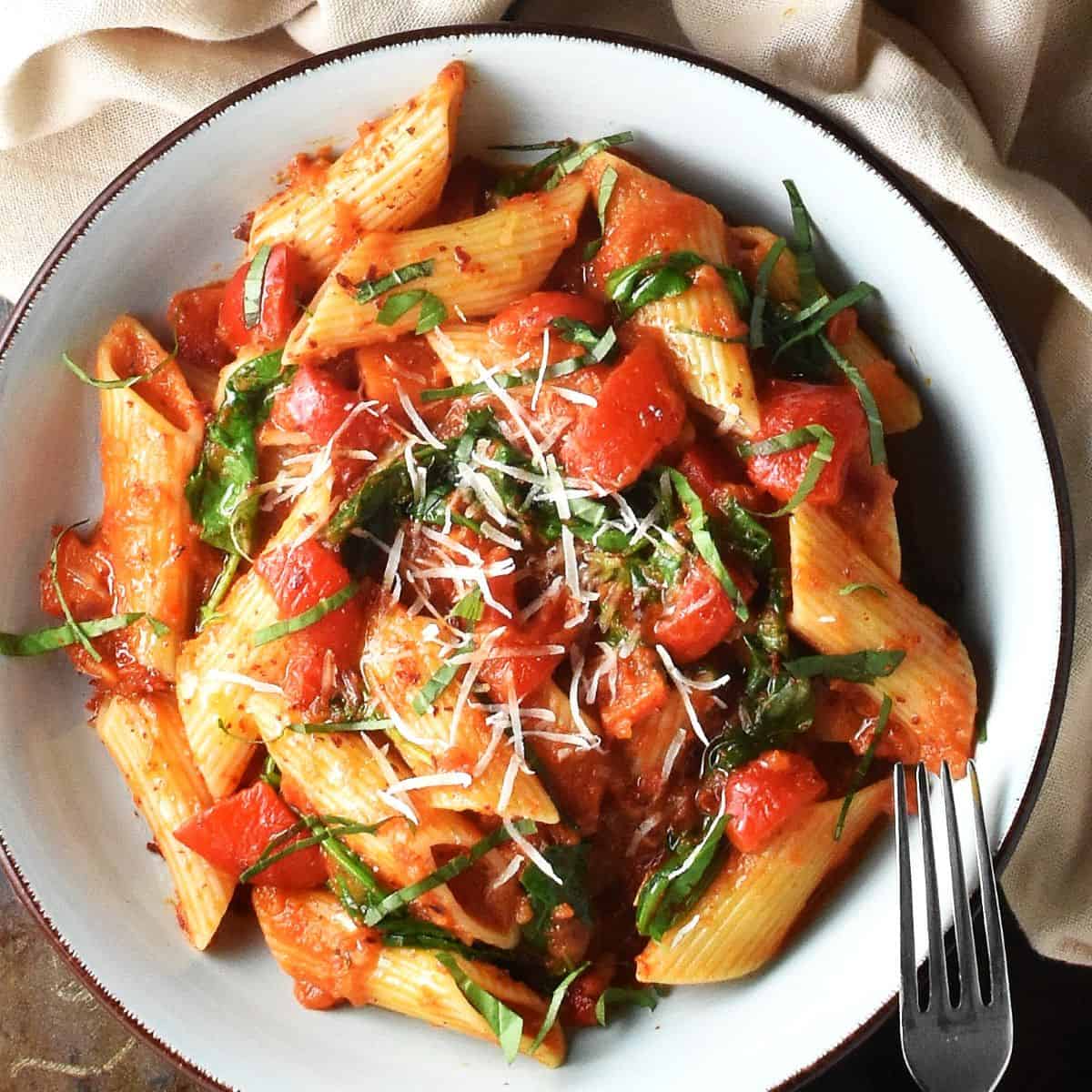 Top down view of red pepper tomato pasta sauce with rigatoni pasta in blue bowl with fork.