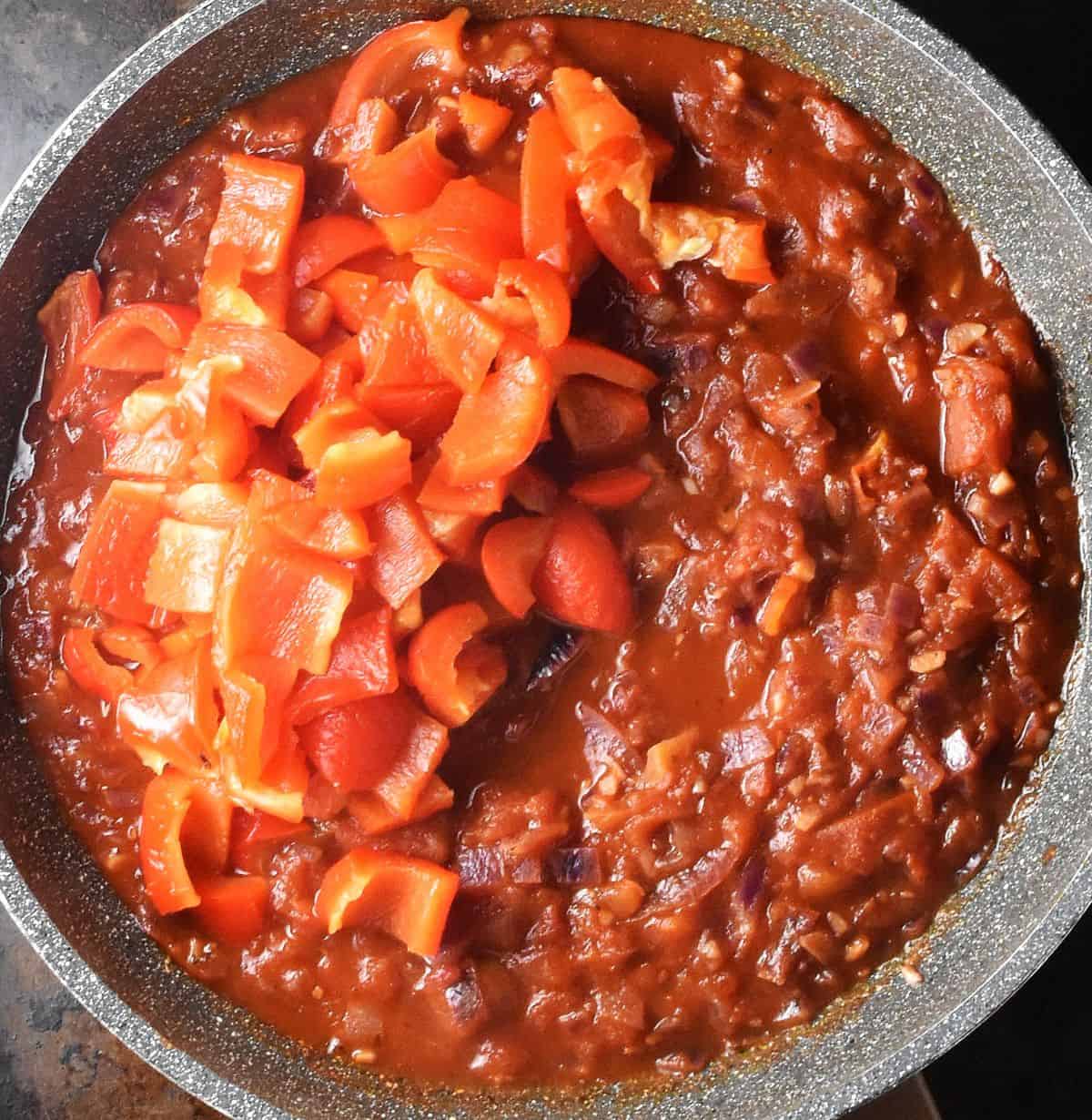 Chunks of roasted red peppers and thick tomato sauce in large pan.