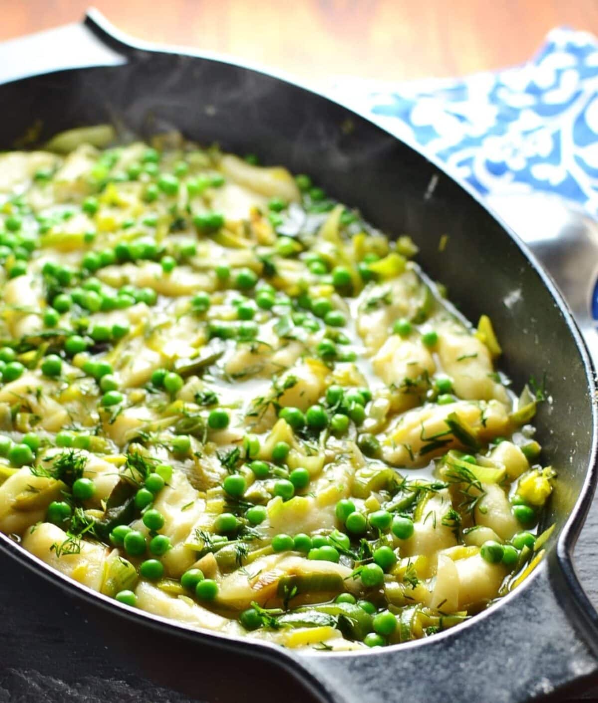 Leek stew with potato dumplings in black cast iron oval casserole dish with steam visible and blue-and-white cloth in background.