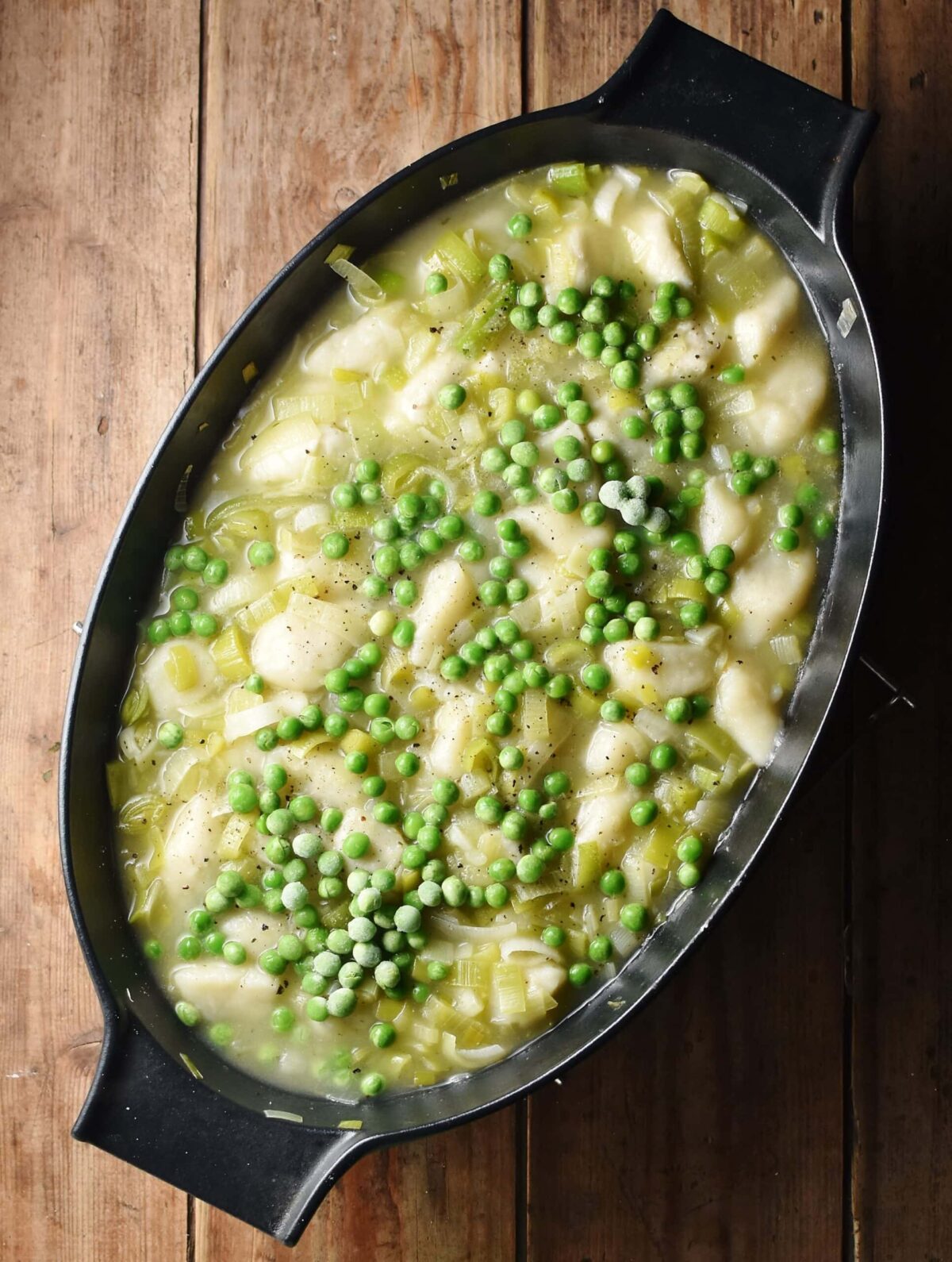 Leek and potato dumpling stew with peas in large, oval, black, shallow dish.