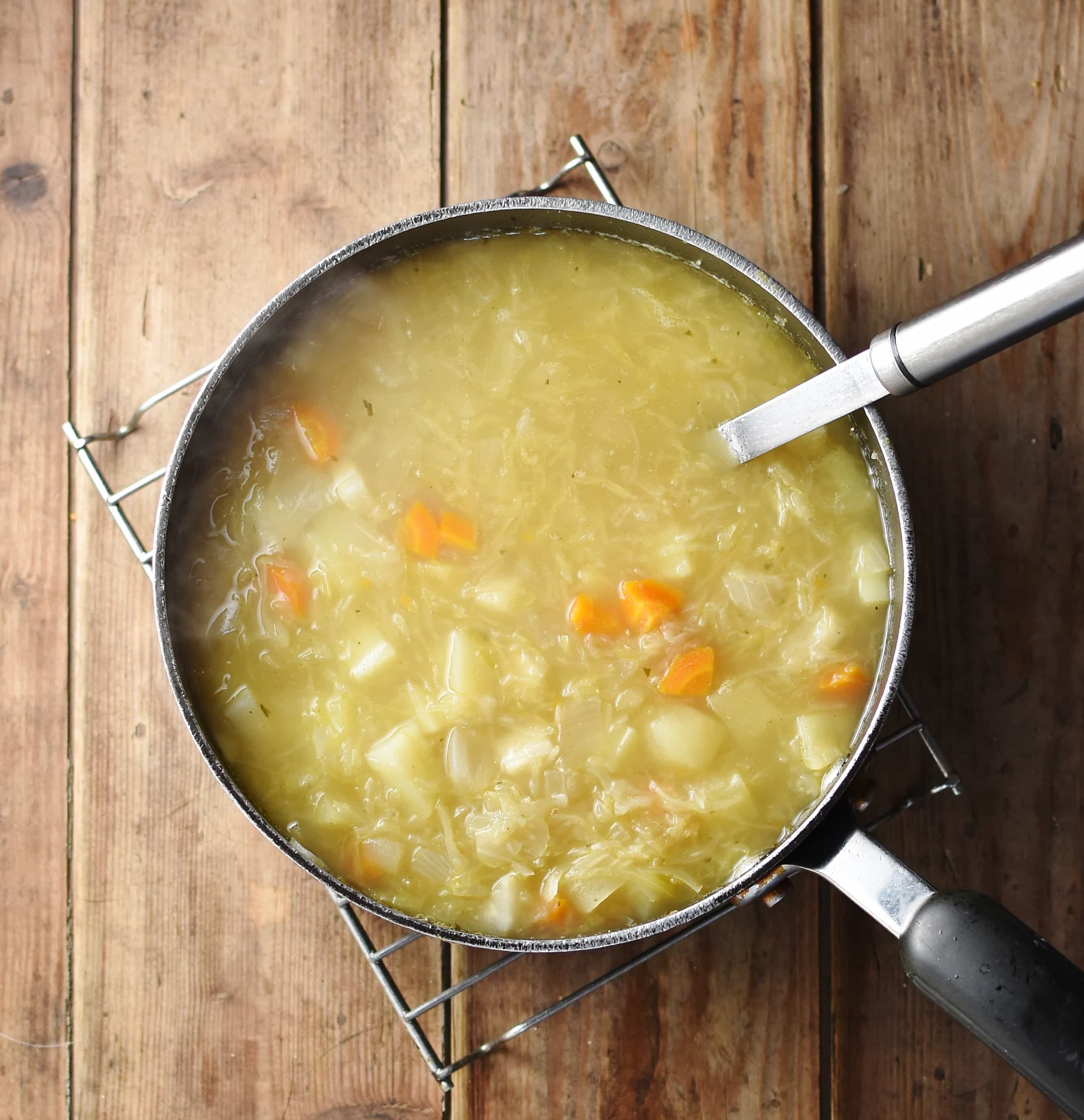 Sauerkraut soup with potatoes and carrots in large pot with spoon.