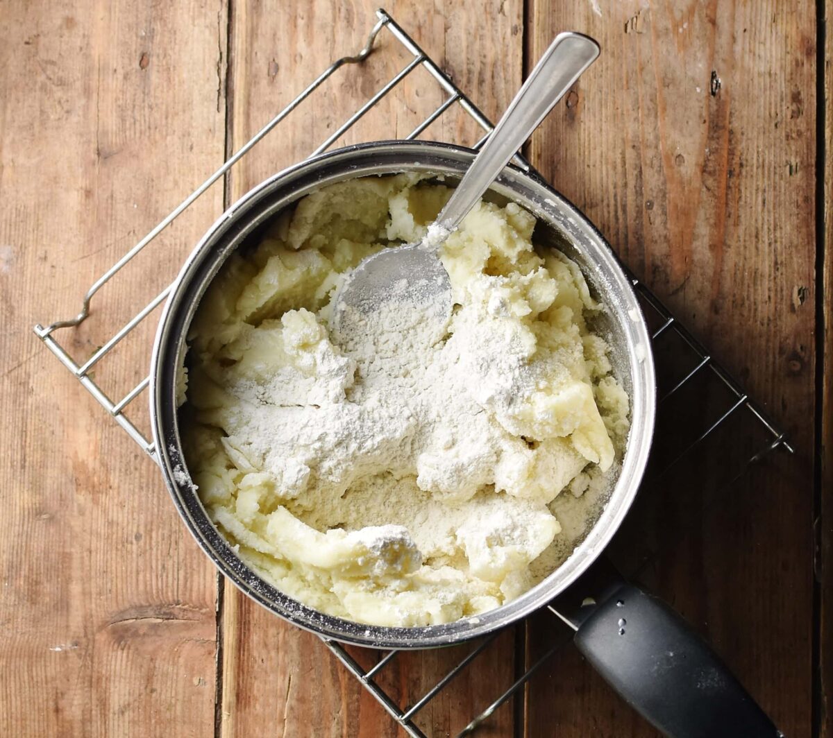 Mashed potatoes with flour and large spoon in pot.