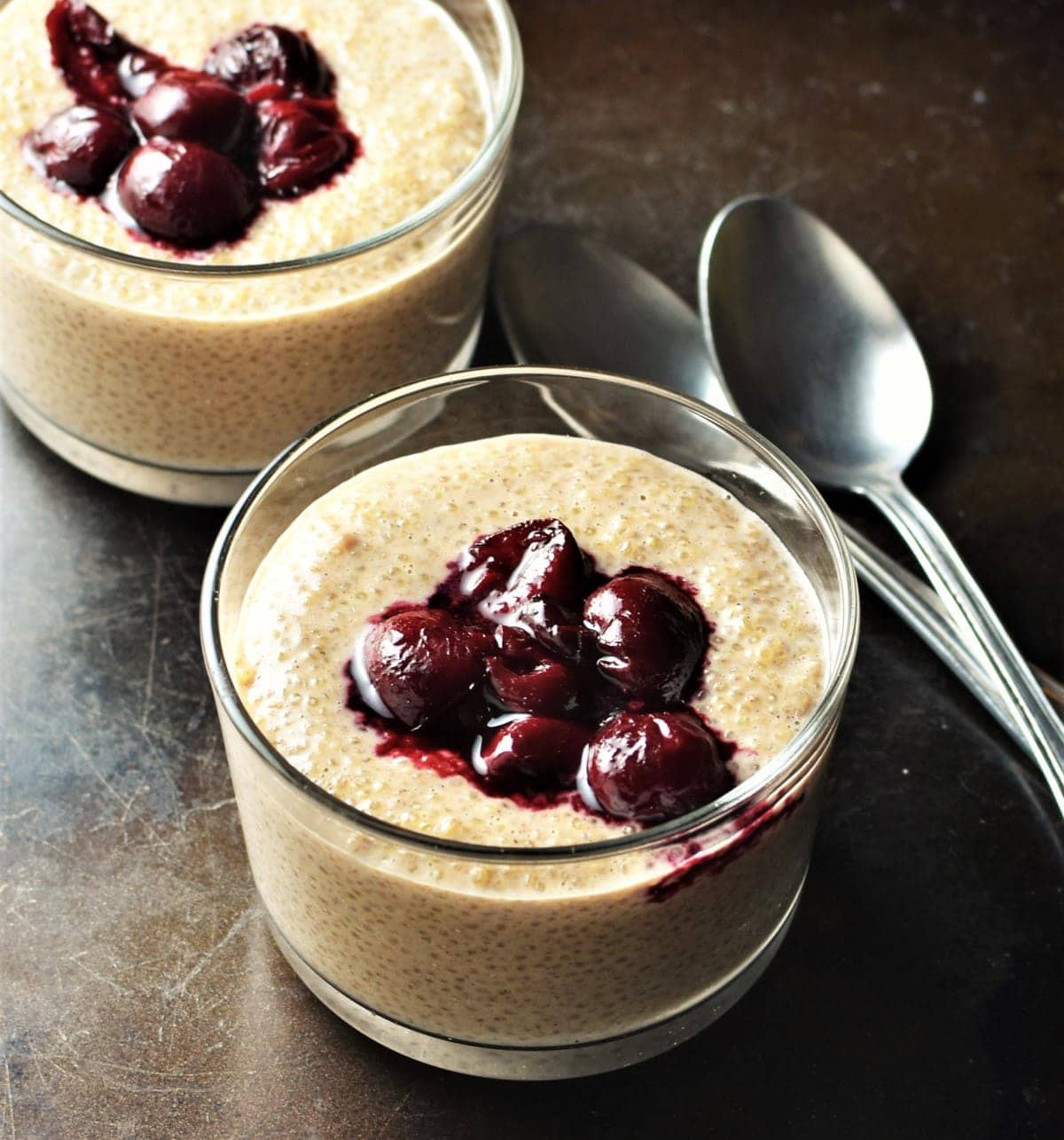 Quinoa pudding with fruit compote in 2 dishes with spoons in background.