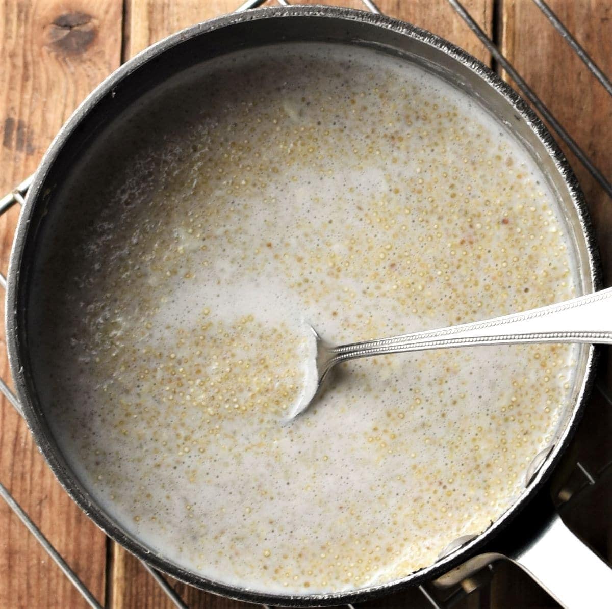 Quinoa pudding in saucepan with spoon.