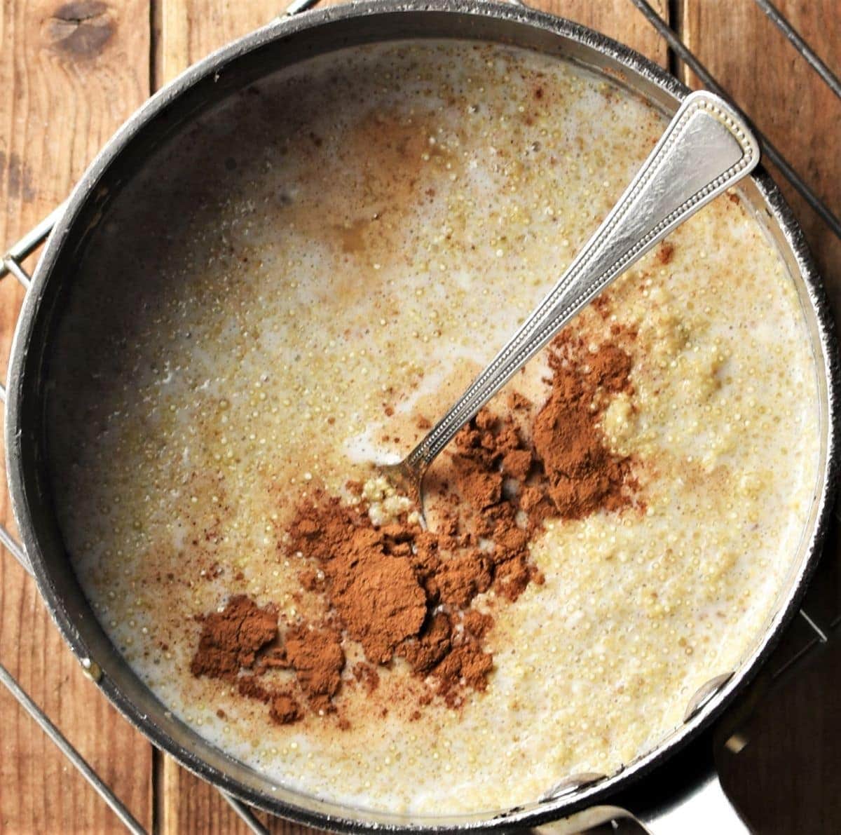 Creamy quinoa pudding with spice in pot with spoon.