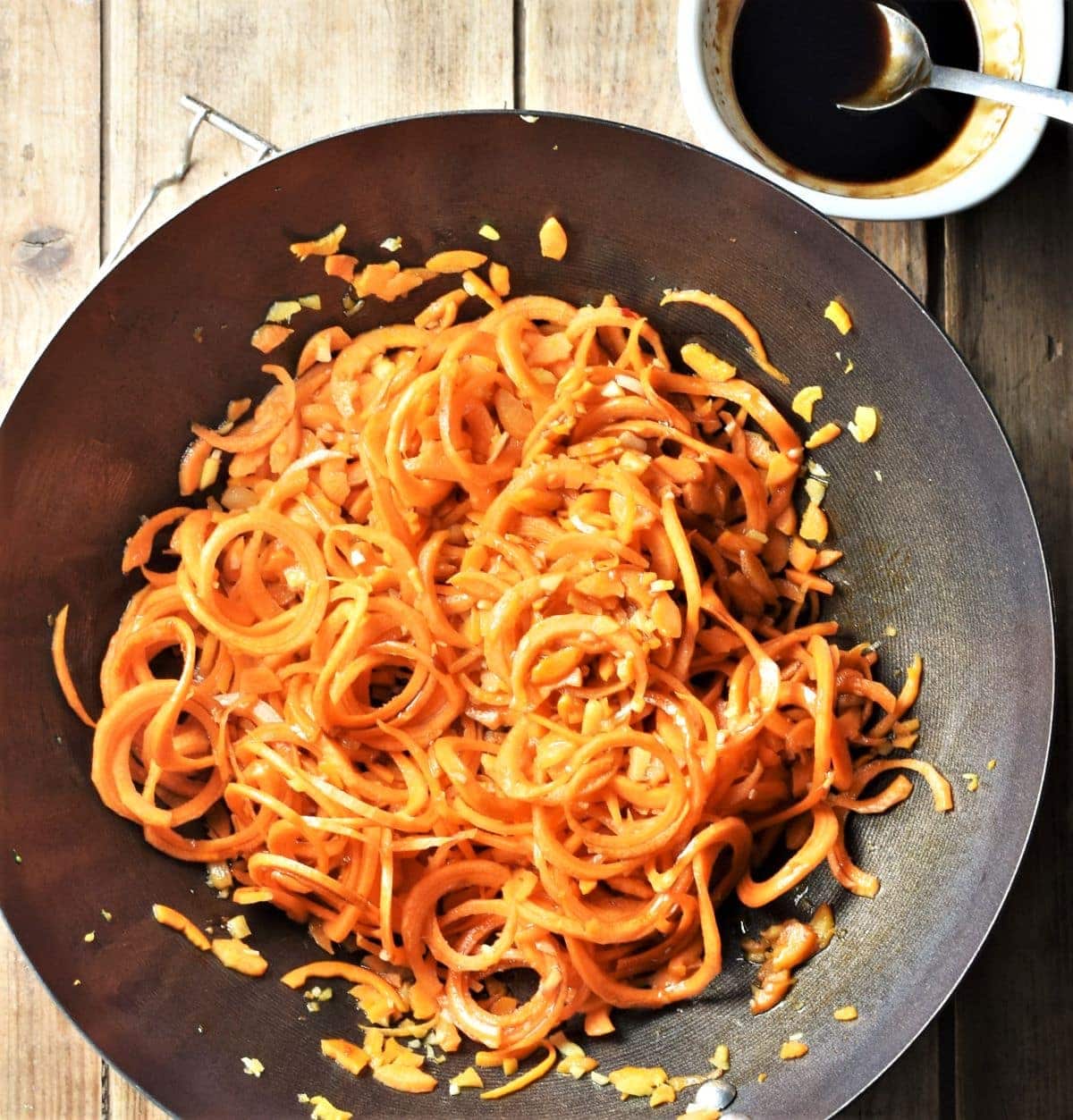 Spiralized carrots in wok with glaze mixture in top tight corner.