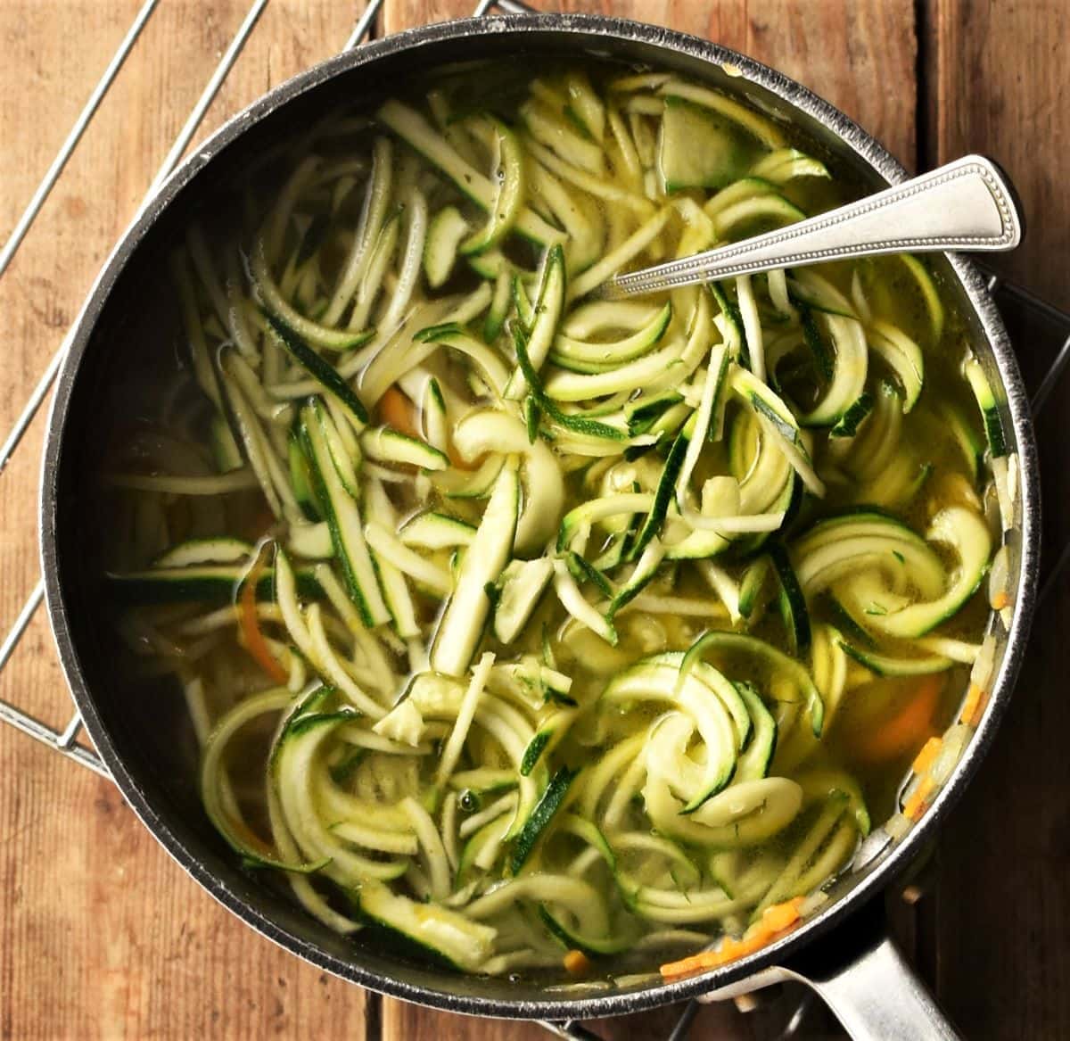 Zucchini noodles in pot with broth and spoon.