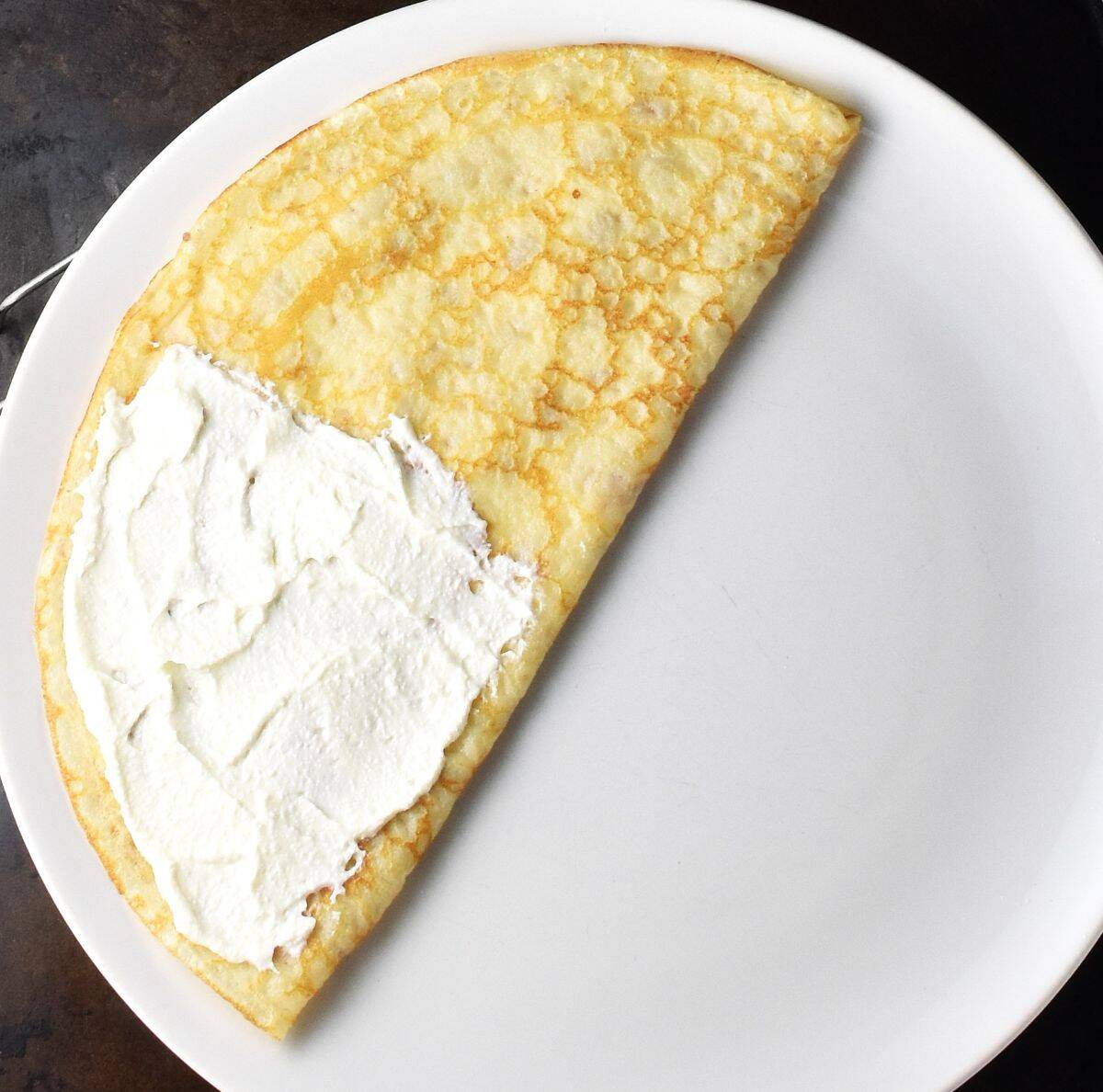 Polish crepe folded in half with creamy cheese on top on white plate.