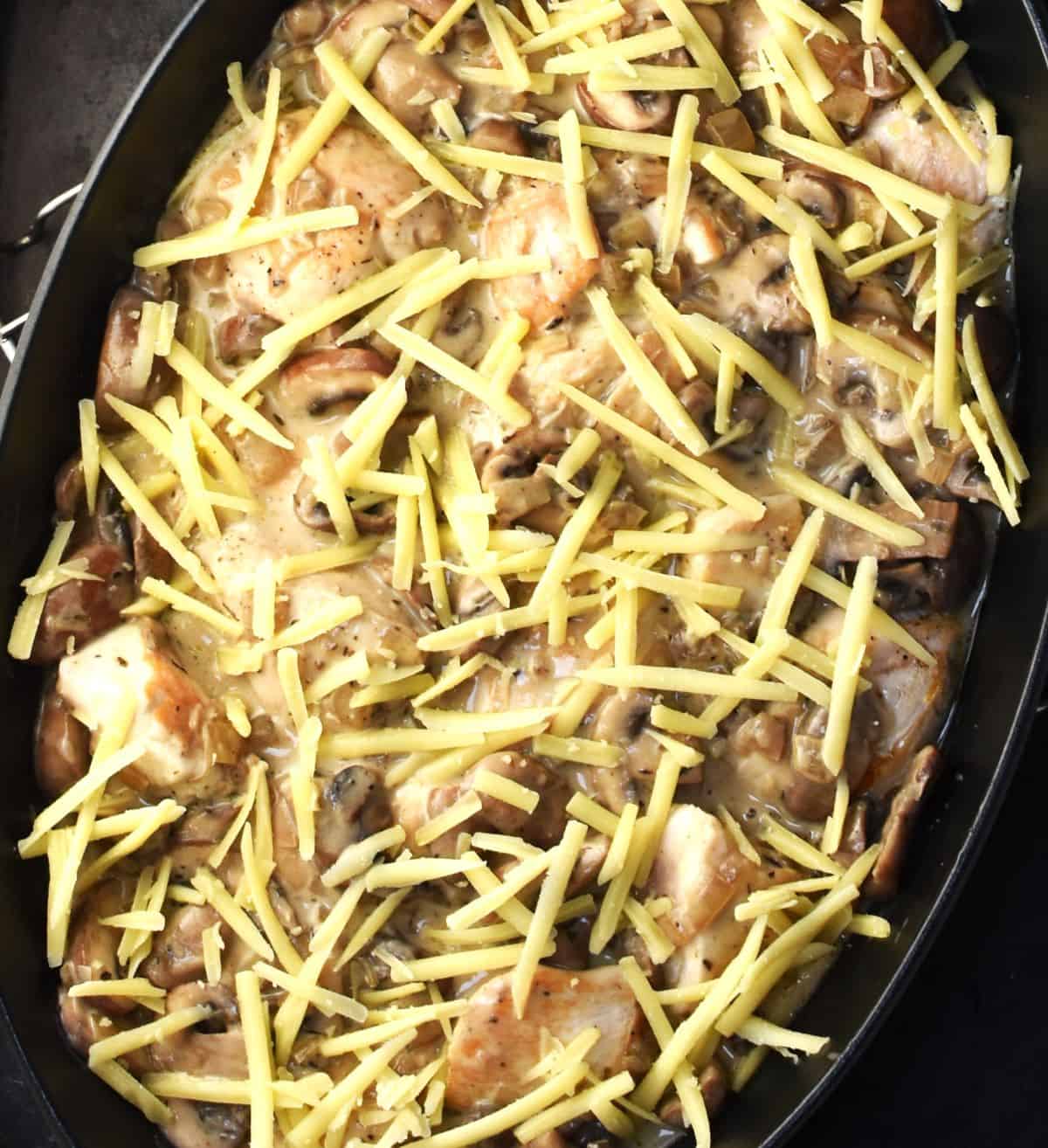 Mushroom chicken casserole in oval dish with grated cheese on top.