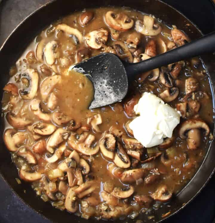 Top down view of mushroom sauce with cream cheese and black spoon in pan.