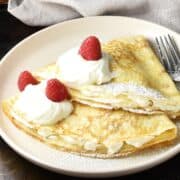 Side view of 2 folded Polish crepes with sour cream and fruit on pink plate.