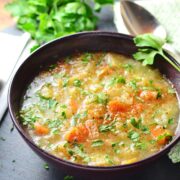 Sauerkraut vegetable soup in purple bowl with white cloth with knife, spoon and parsley.