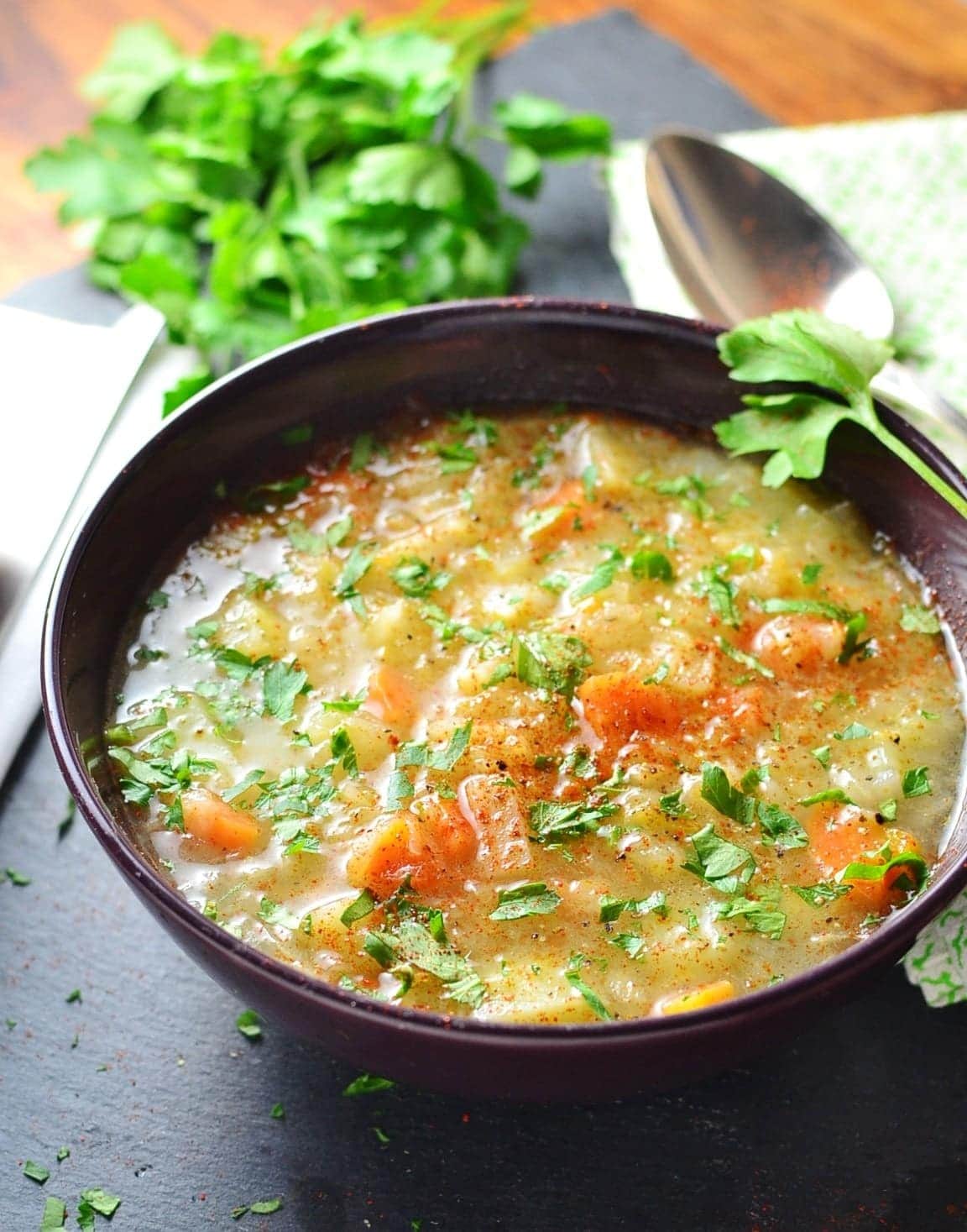 Sauerkraut vegetable soup in purple bowl with white cloth with knife, spoon and parsley.