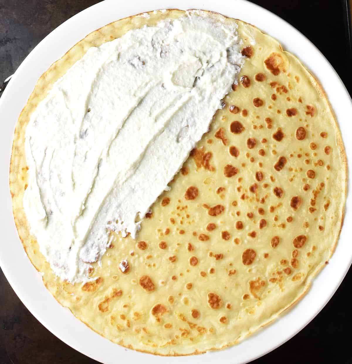 Polish nalesnik covered partly with cheese filling on white plate.