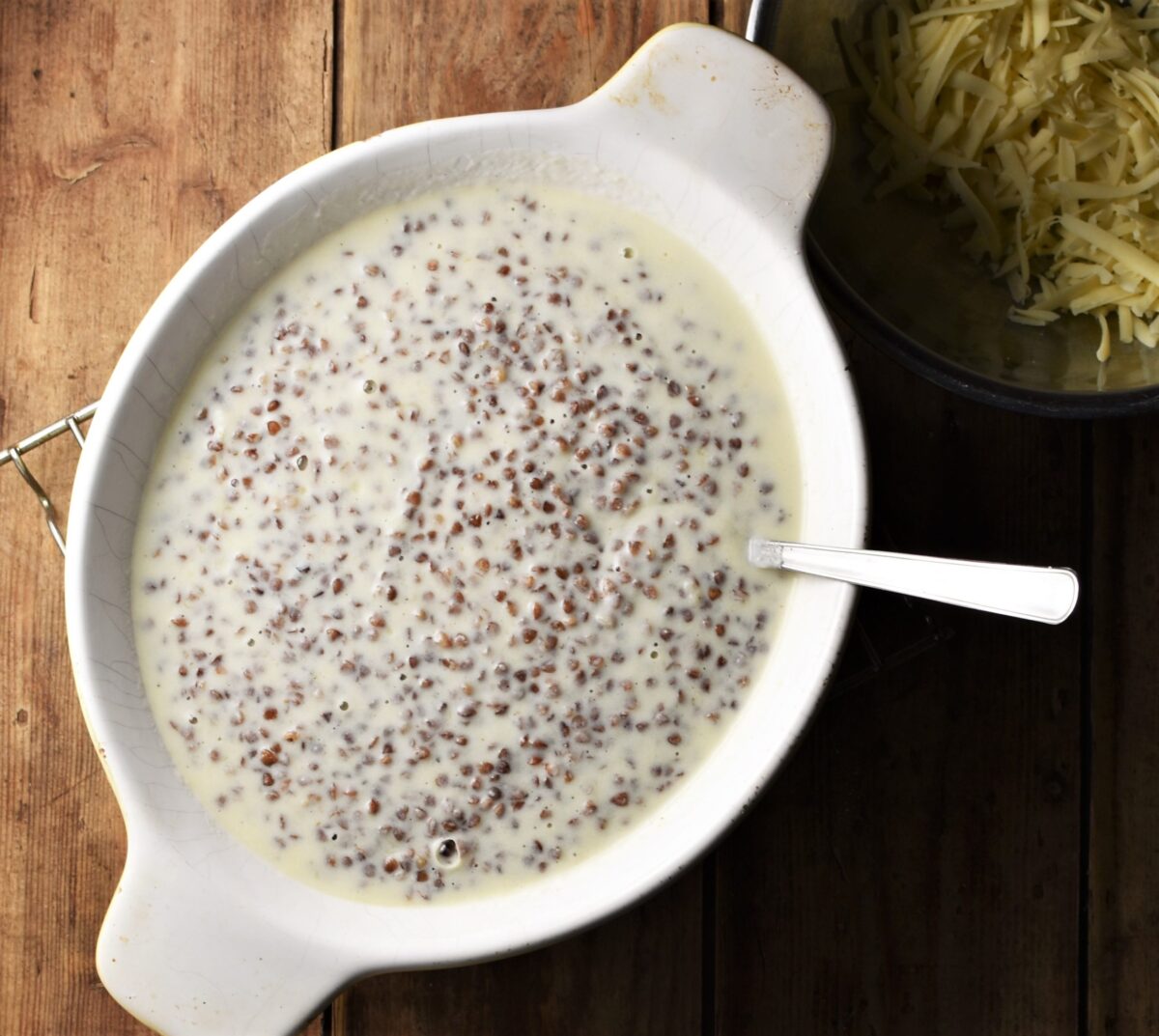 Buckwheat groats in white sauce in oval white dish with spoon.
