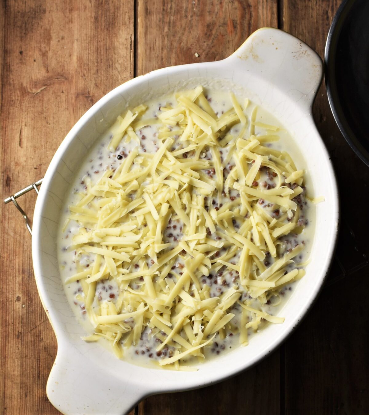 Buckwheat in white sauce with grated cheese on top in white oval dish.