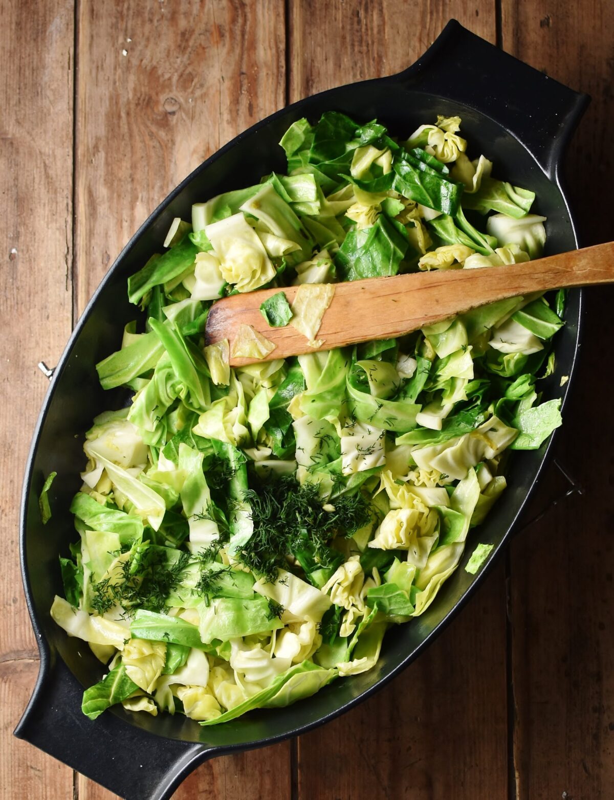 Chopped cabbage in black oval dish with wooden spoon.
