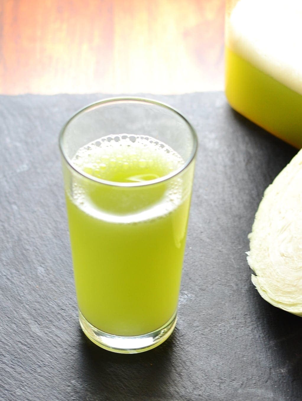 Cabbage juice in glass with melon and cucumber on slate surface.