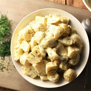 Creamy potato dill salad in white bowl with dill to the left.