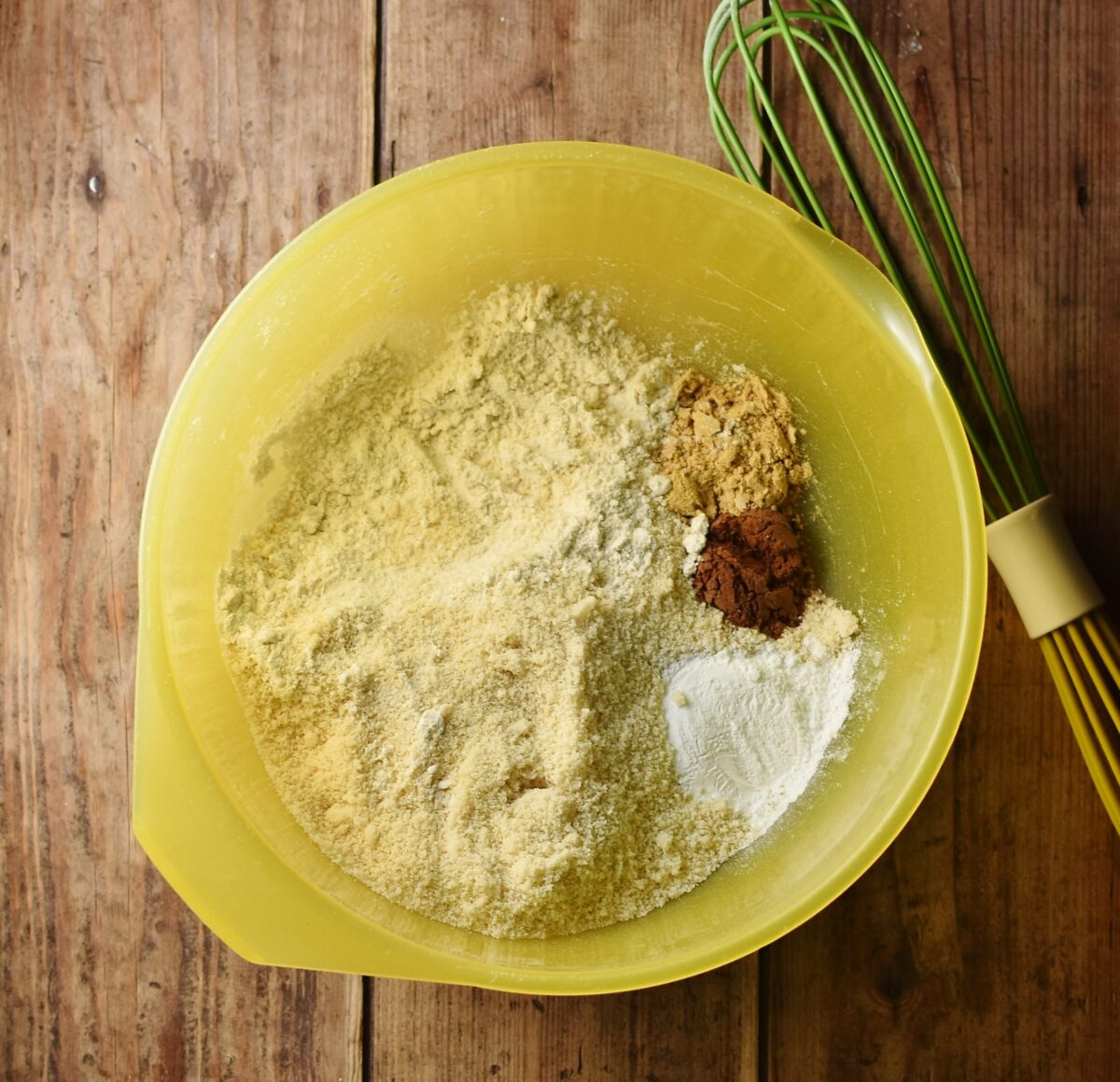 Flour and spice in large yellow bowl with green whisk.