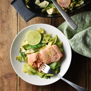 Salmon with chopped cabbage and fork in white bowl, with green cloth and black dish with salmon in background.