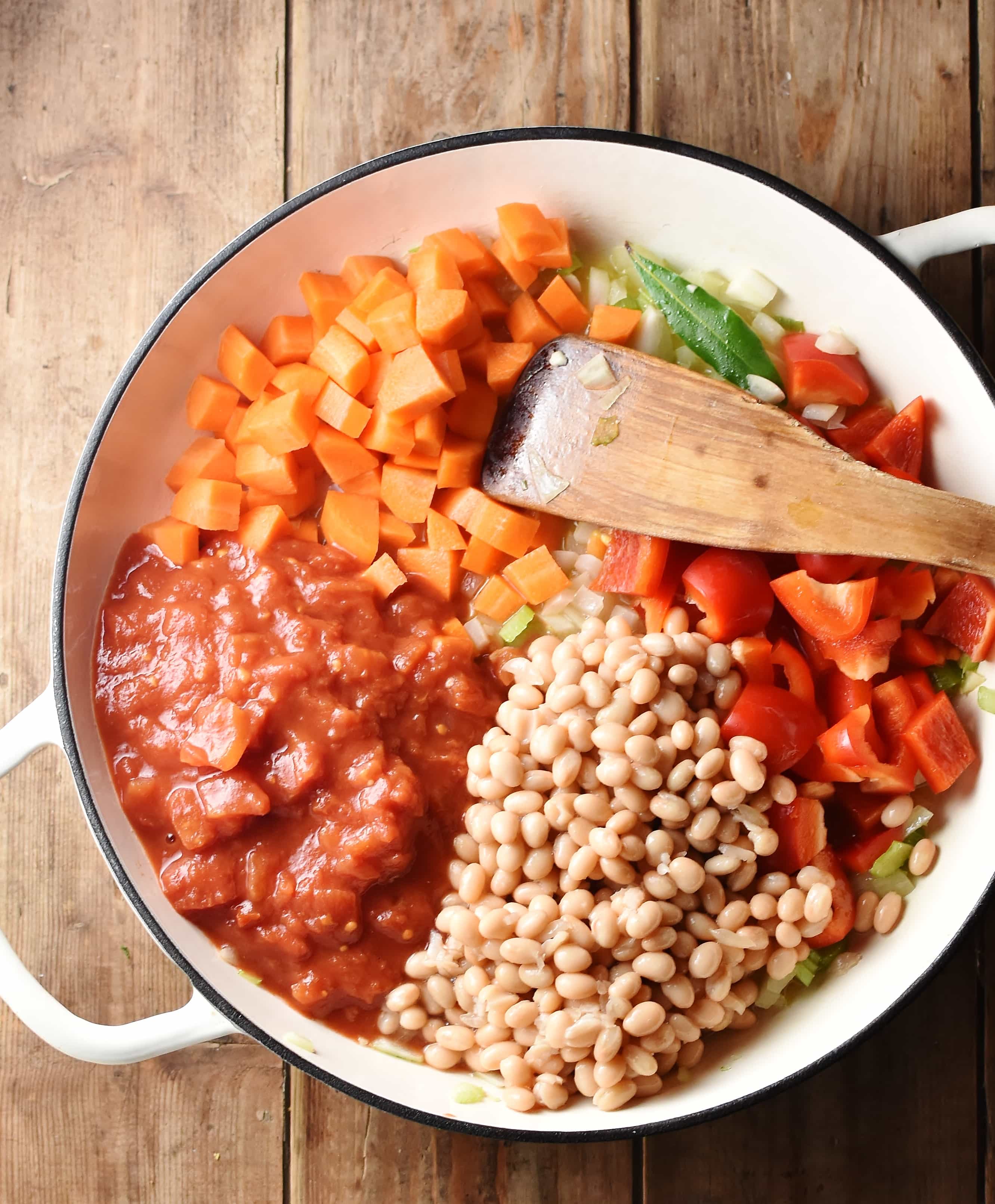 Beans, tomatoes, diced carrots and chopped red pepper in large shallow white dish with wooden spatula.
