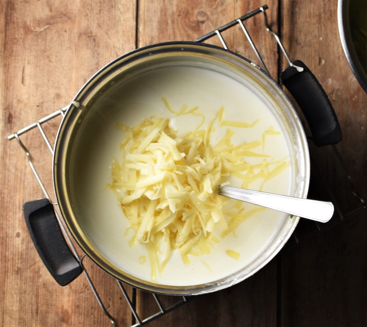 White sauce and grated cheese in pot with spoon.