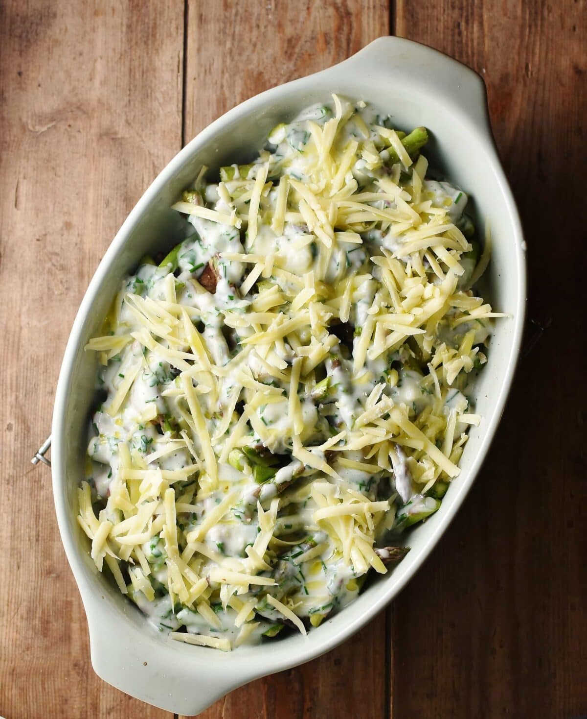 Asparagus casserole with grated cheese on top in green oval dish. 