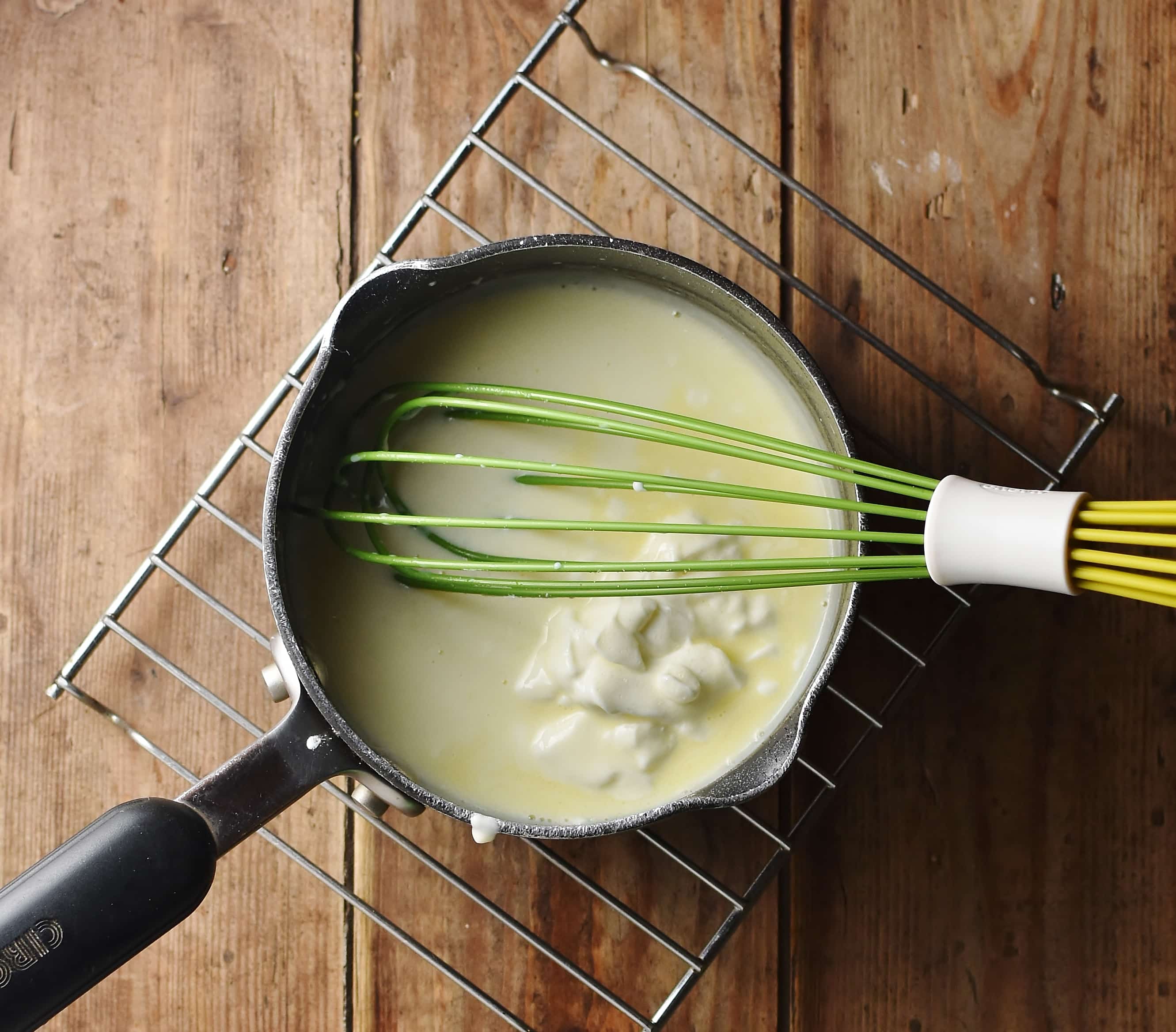 White sauce with yogurt and green whisk in saucepan.