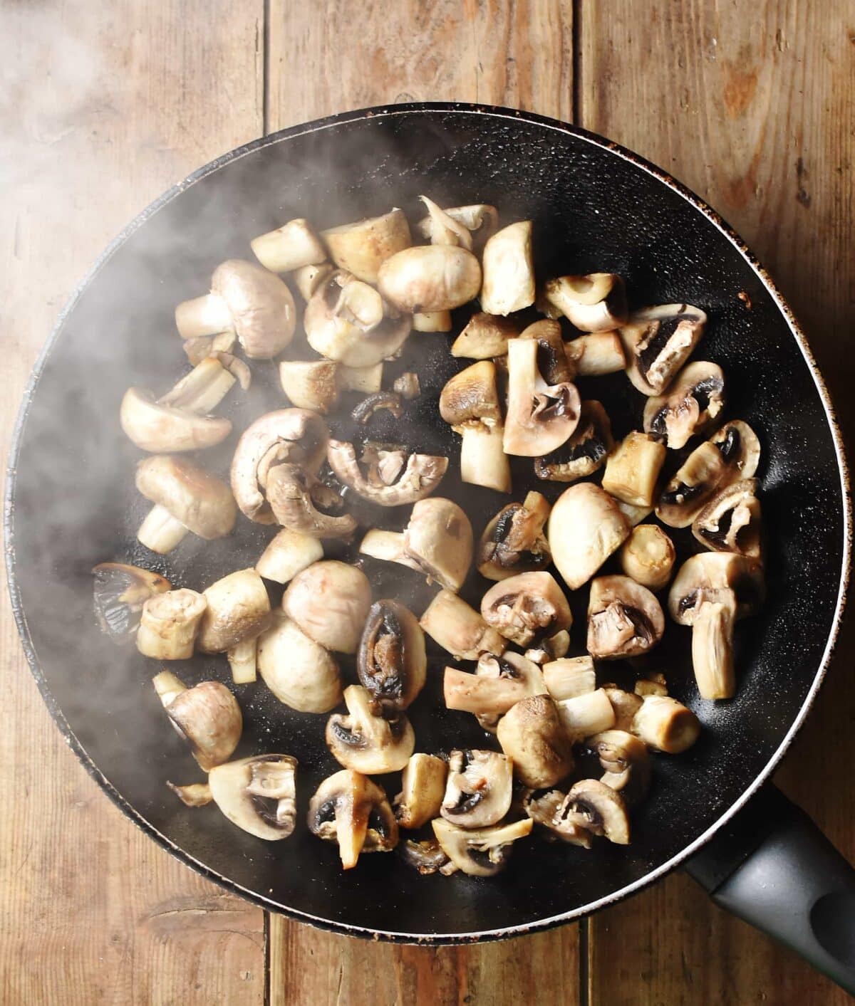 Chopped mushrooms in large pan with steam visible.