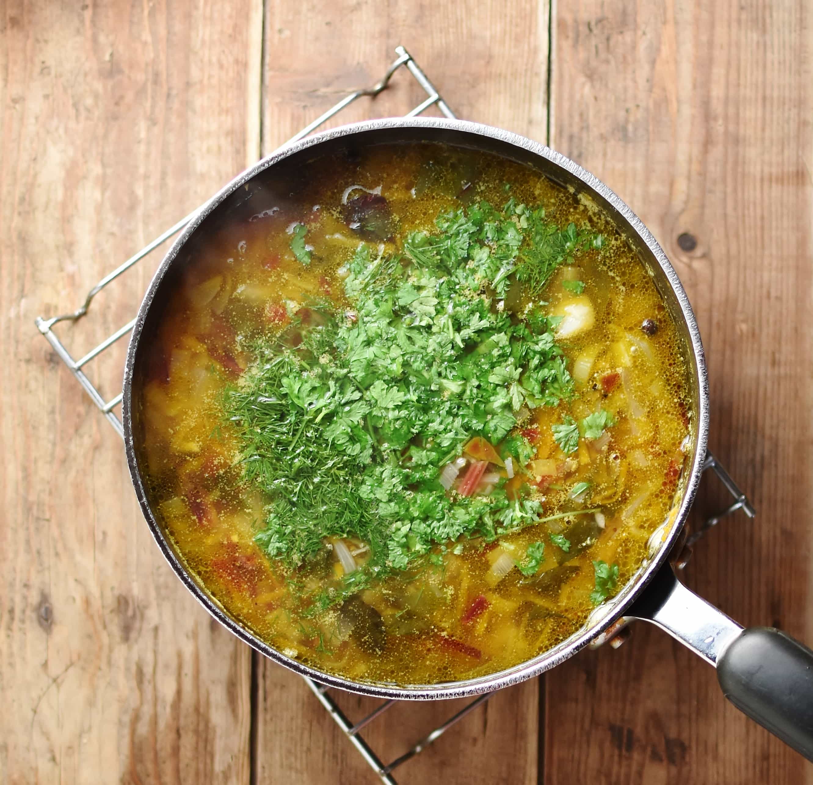 Soup with fresh herbs inside large pot.