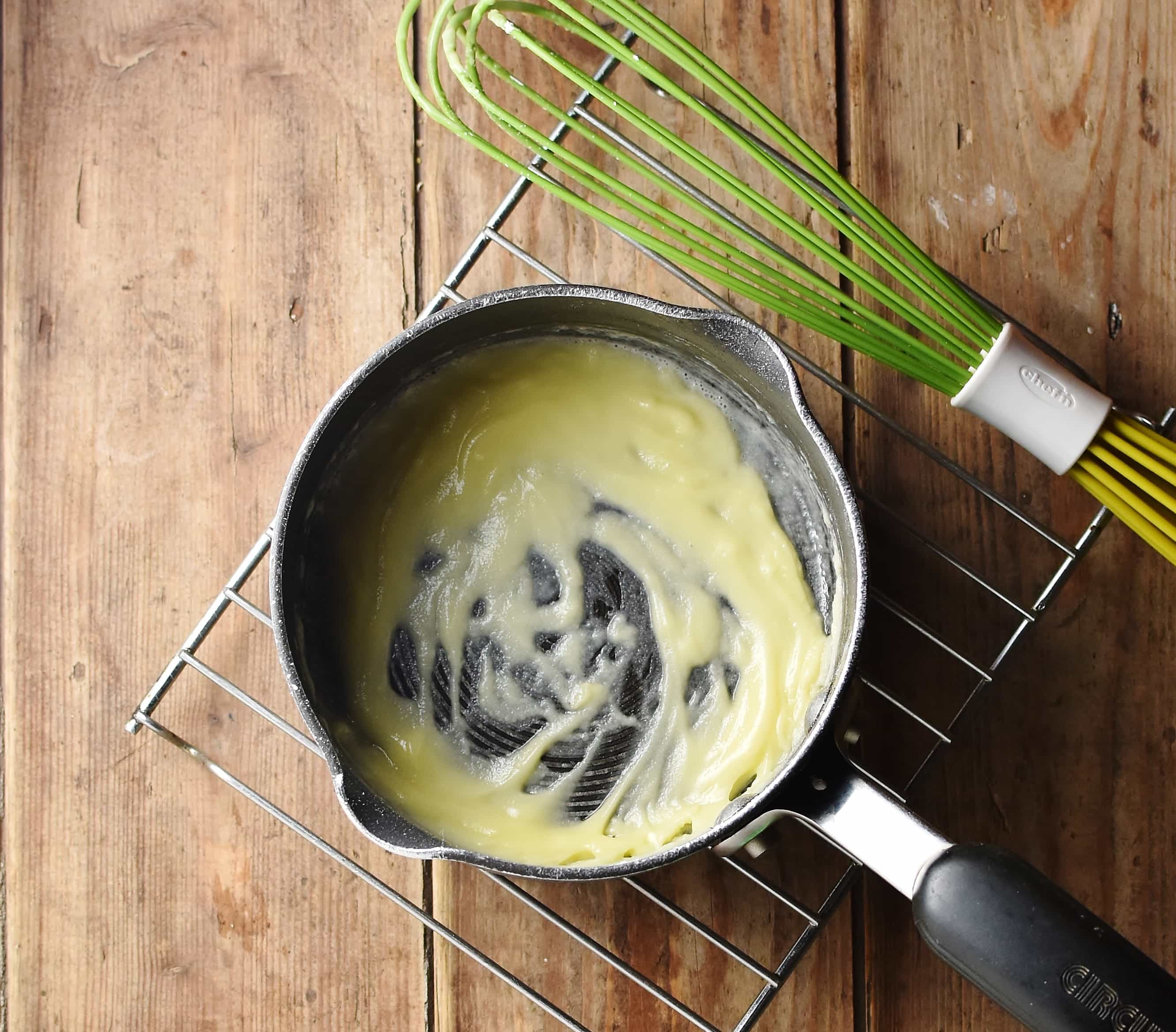 Roux in saucepan on top of rack with green whisk to the right.