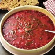 Side view of beet greens soup in beige bowl with spoon and bread in background.