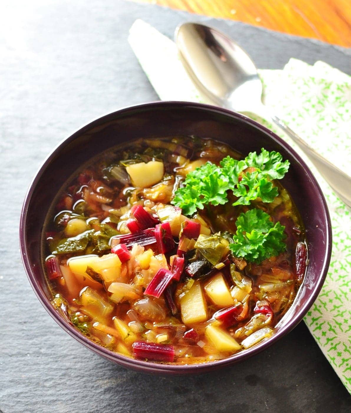 Beet greens vegetable soup in purple bowl with green cloth and spoon.