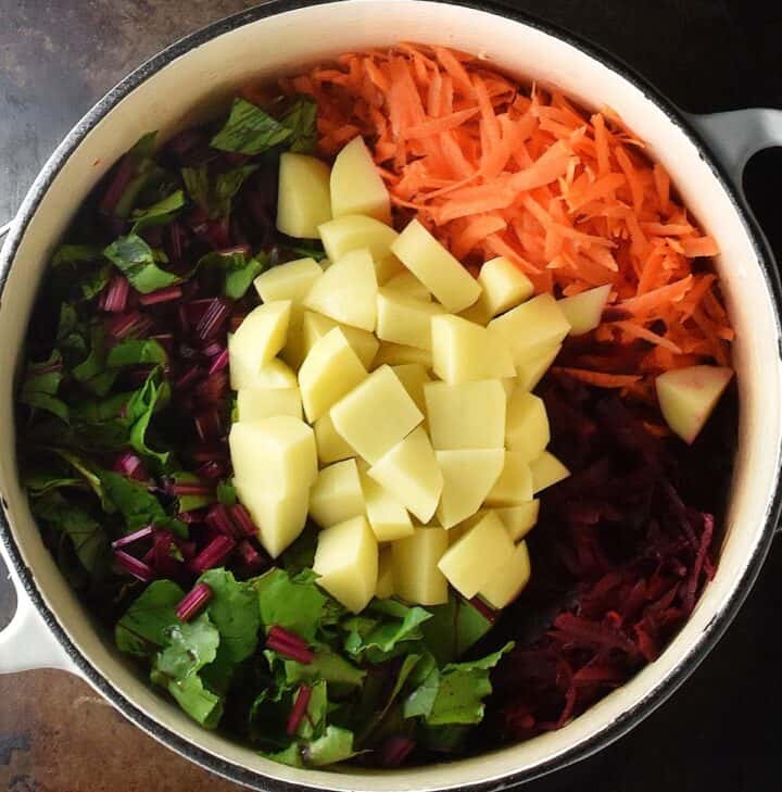 Shredded and cubed vegetables in large white pot.
