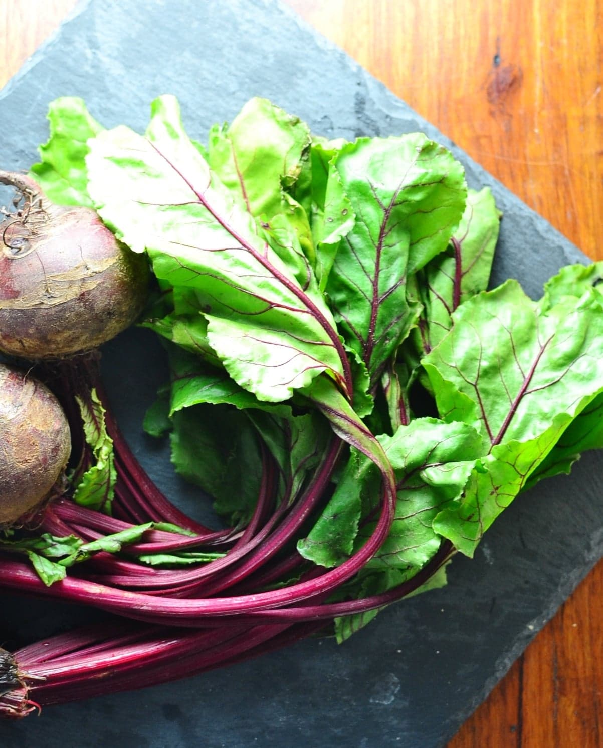 Beet greens with beetroot on square slate surface.