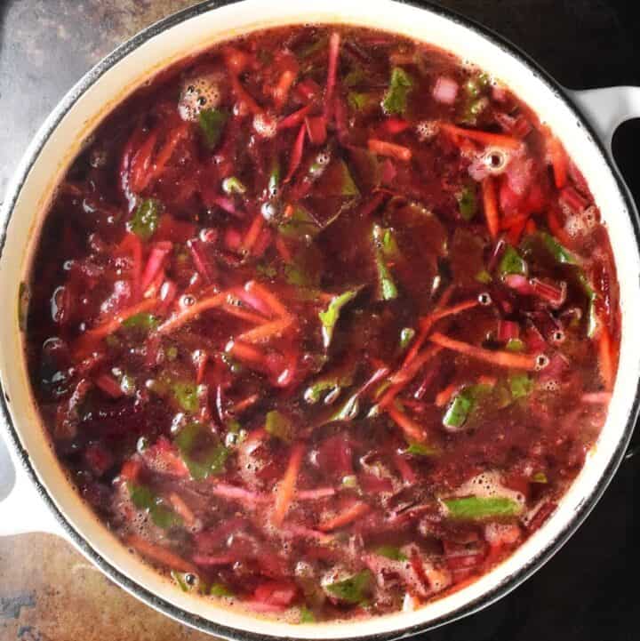 Soup with shredded vegetables and green beans in white pot.