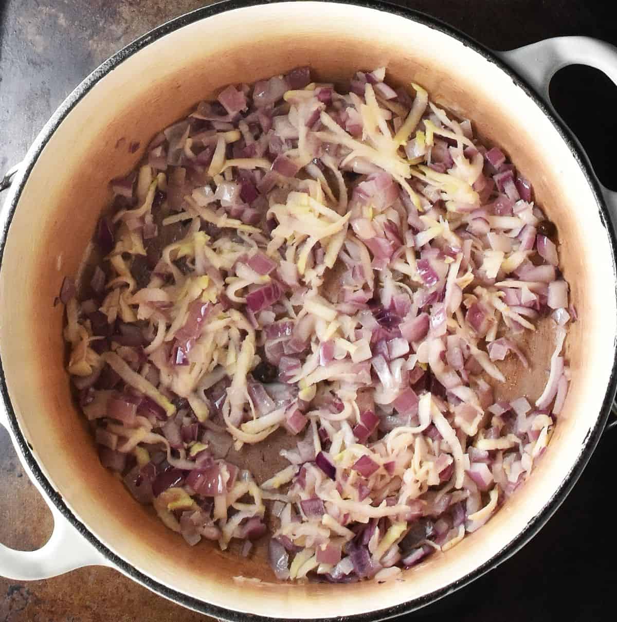 Top down view of chopped red onion and shredded celeriac in white pot.