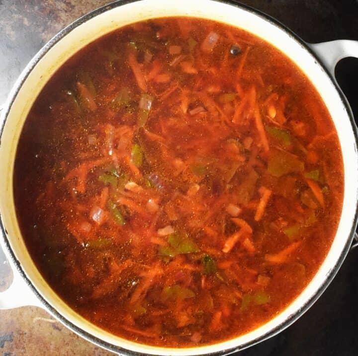 Top down view of cooked beet greens soup in large white pot.