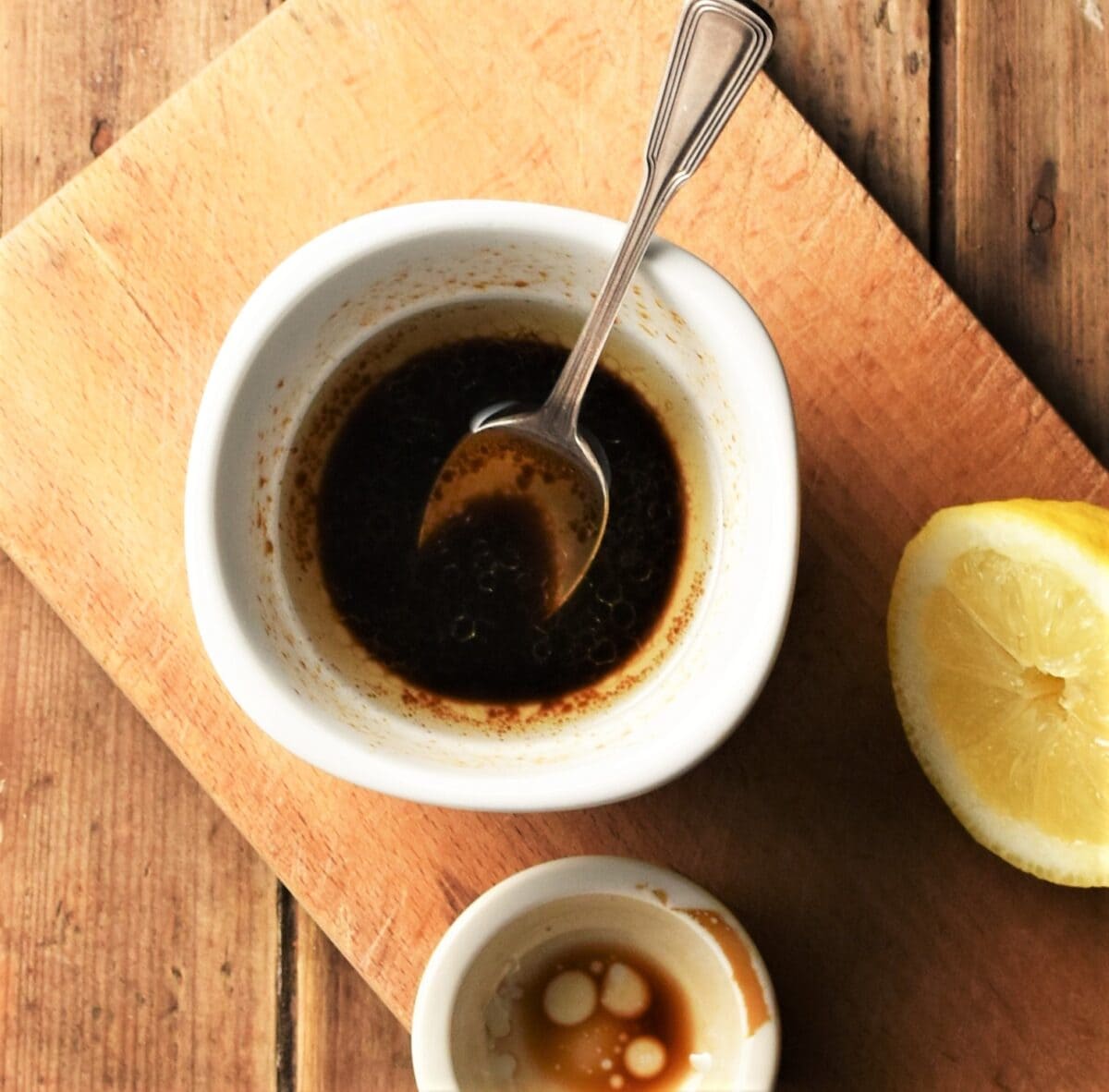 Balsamic dressing in white bowl with spoon on top of wooden board.