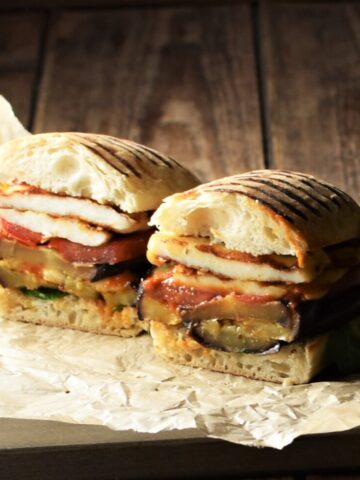 Side view of eggplant sandwich cut in half on top of paper.