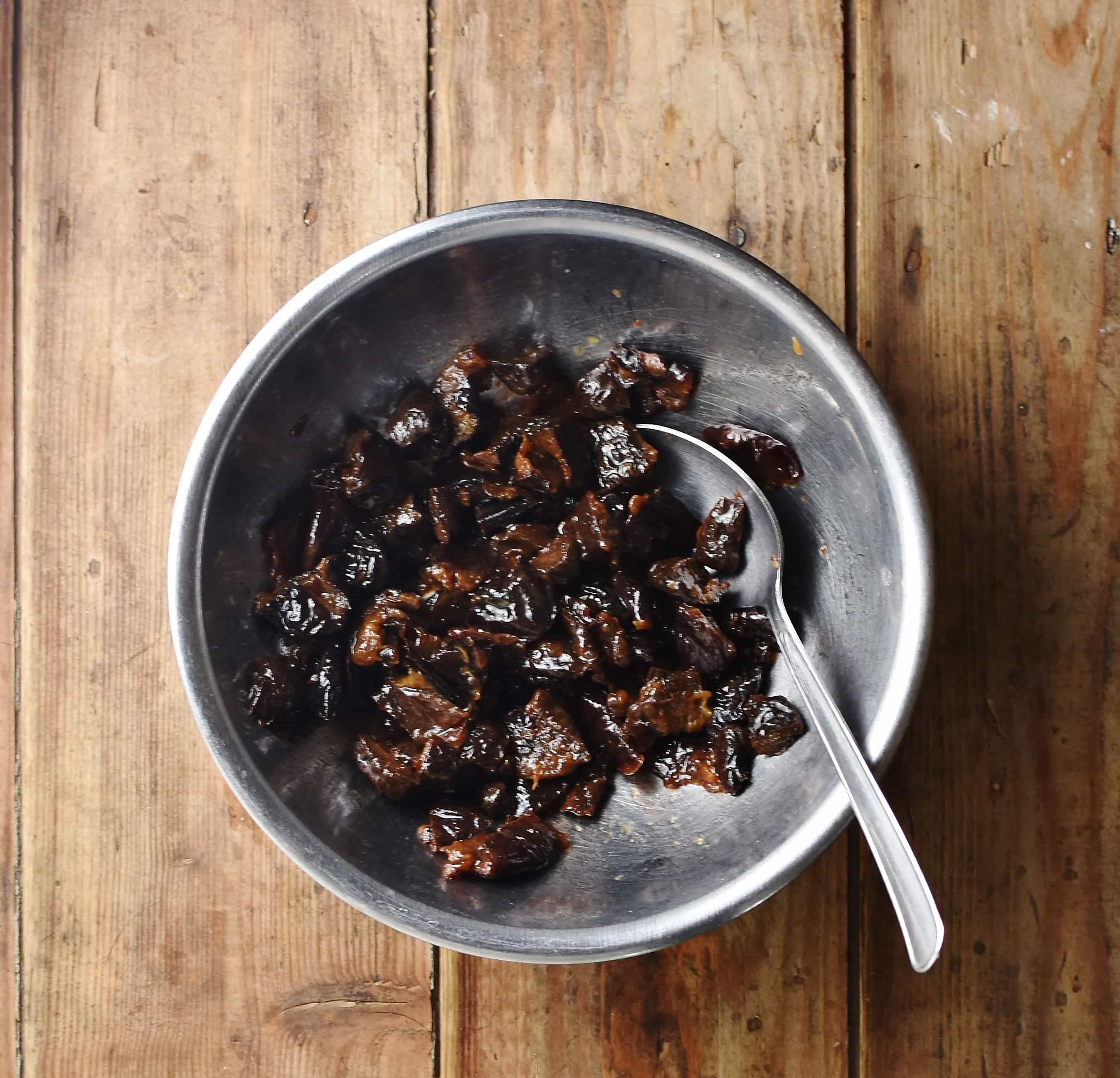 Chopped prunes in large metal bowl with spoon.