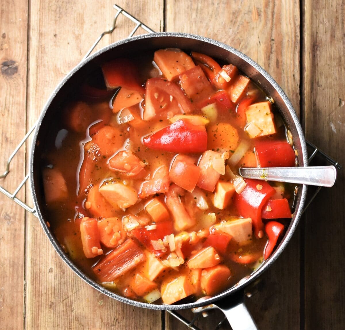 Chopped sweet potato, red pepper and carrot with stock in large pot with spoon.