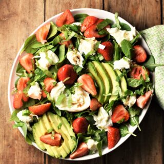Top down view of strawberry and spinach salad with avocado and mozzarella on white plate.