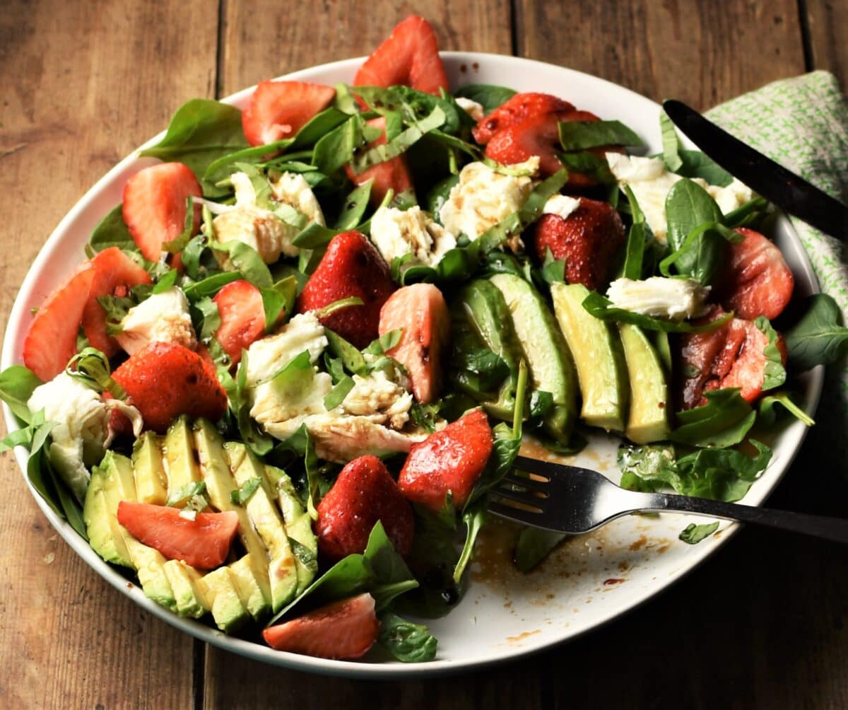 Avocado, strawberries, spinach and strawberry salad on white plate with fork.