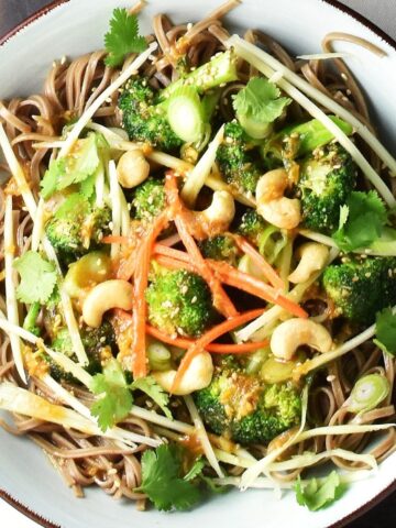 Top down view of broccoli and noodle salad with herbs, vegetables and nuts in blue bowl.