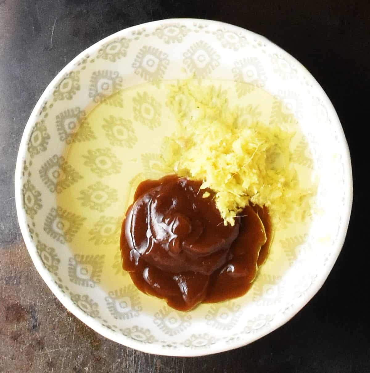 Top down view of oil, hoisin sauce and fresh grated ginger in grey bowl.