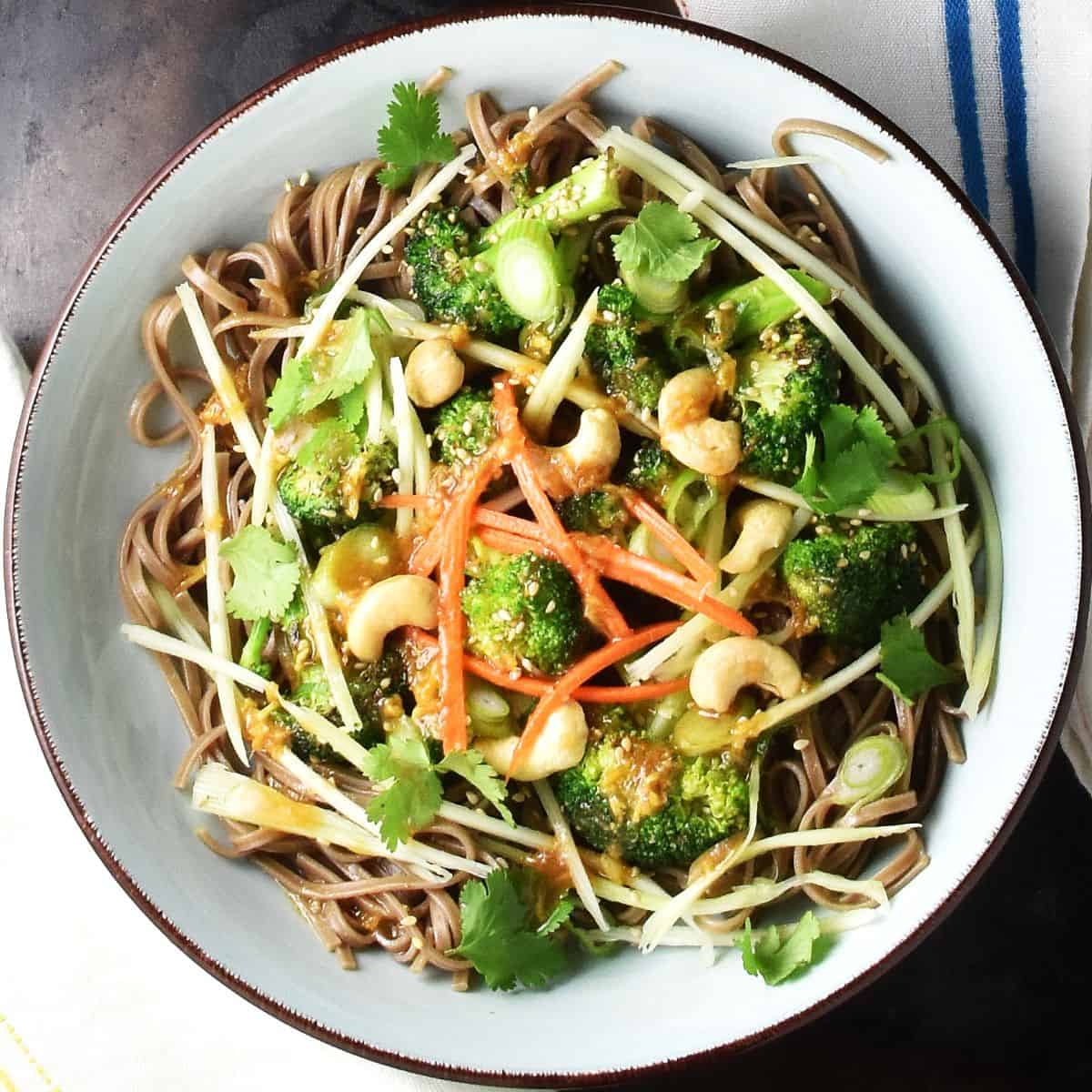 Top down view of broccoli noodle salad with shredded vegetables in blue bowl.